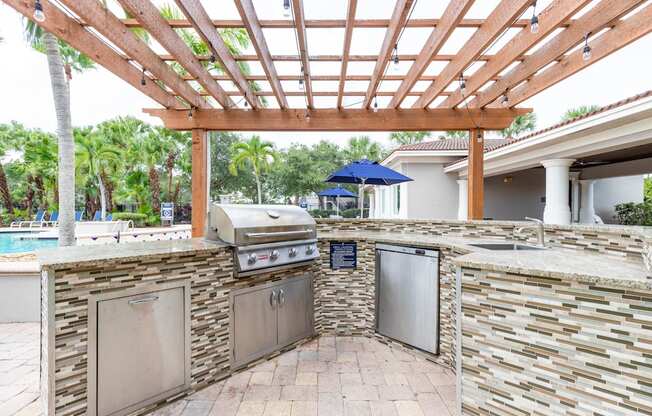 an outdoor kitchen with a pergola and a pool in the background at Heritage Bay, Florida, 34957