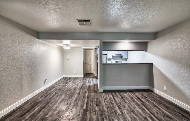 an empty living room with a kitchen in the background