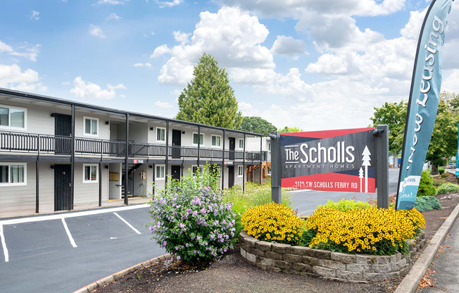A sign for The Scholls apartment complex is in front of a building.