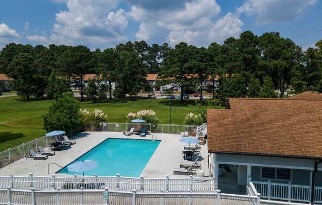 A pool surrounded by a white fence with trees in the background.
