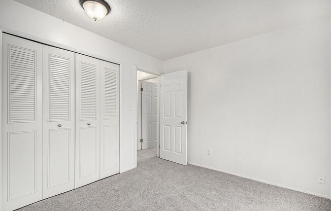 an empty bedroom with white closet doors and a door to the bathroom