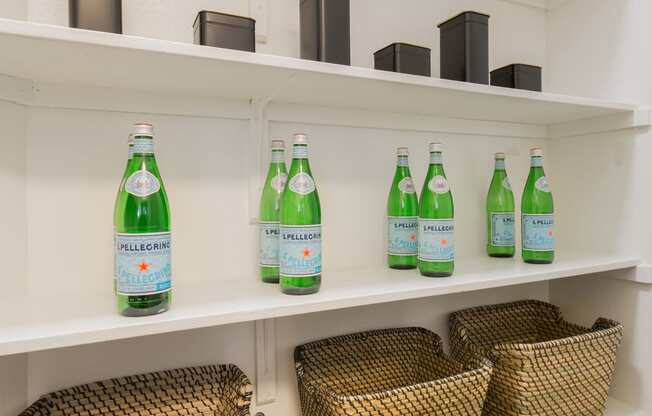 a pantry with white shelves and wicker baskets and green bottles of soda on the shelves