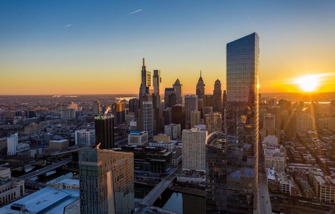 A cityscape with tall buildings and a sunset in the background.