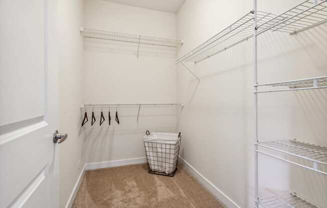 a walk in closet with white walls and shelves and a basket on the floor