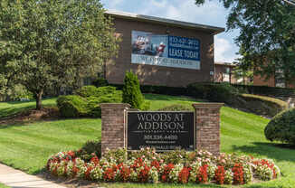 A sign for Woods at Addison with a phone number and a website.