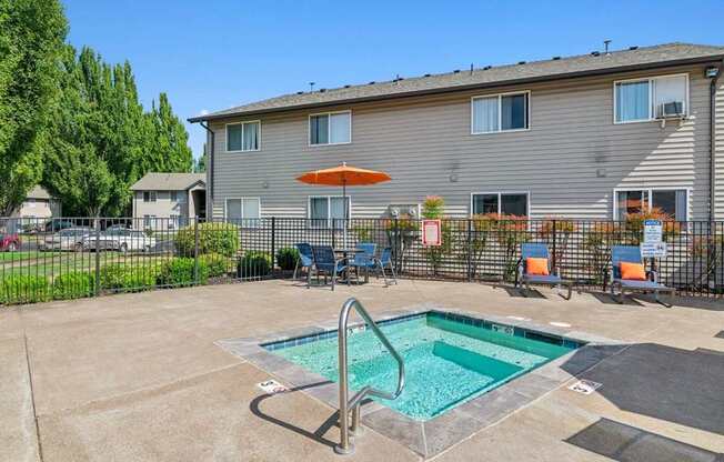 A small pool in a courtyard surrounded by chairs and a building in the background.