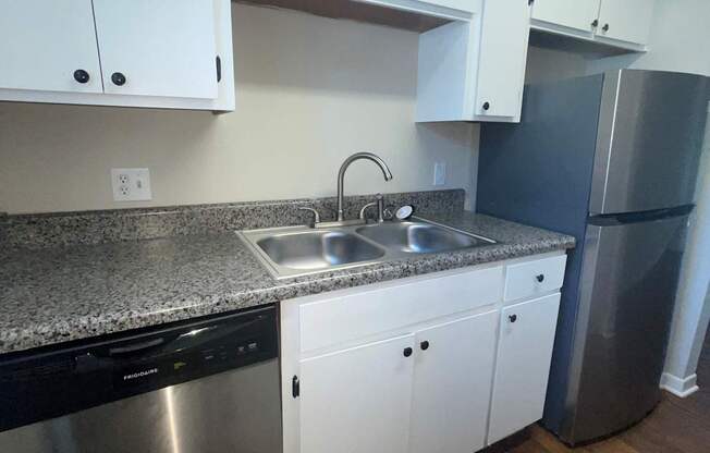 A kitchen with white cabinets and a stainless steel dishwasher and refrigerator.