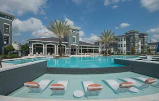 A pool with sun loungers in front of a hotel.