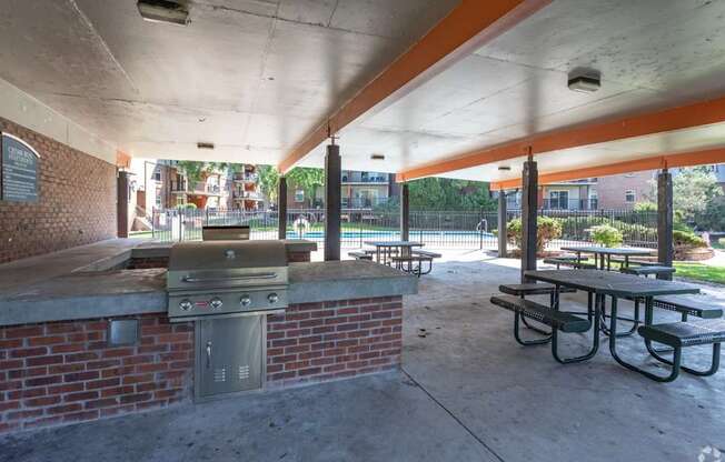 A covered picnic area with a grill and picnic tables.