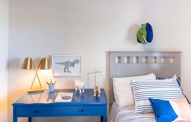 A blue desk with a lamp and a dinosaur picture on the wall.