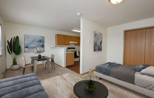 Fargo, ND Ashbury Apartments. a bedroom with a bed a table and a chair and a kitchen in the background