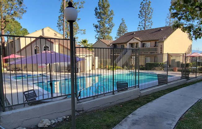 Gated swimming pool, spa, and sun deck area surrounded by lush gardens and trees at Northwood Apartments in Upland, California.