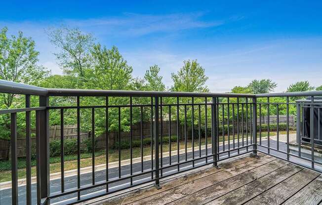 A wooden deck with a metal railing overlooks a road and greenery.