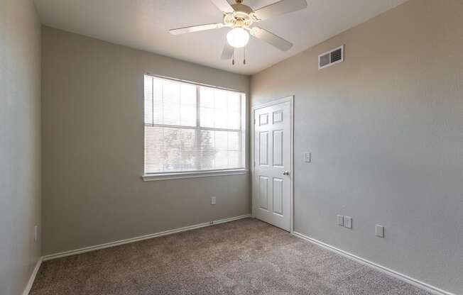 an empty bedroom with a ceiling fan and a window