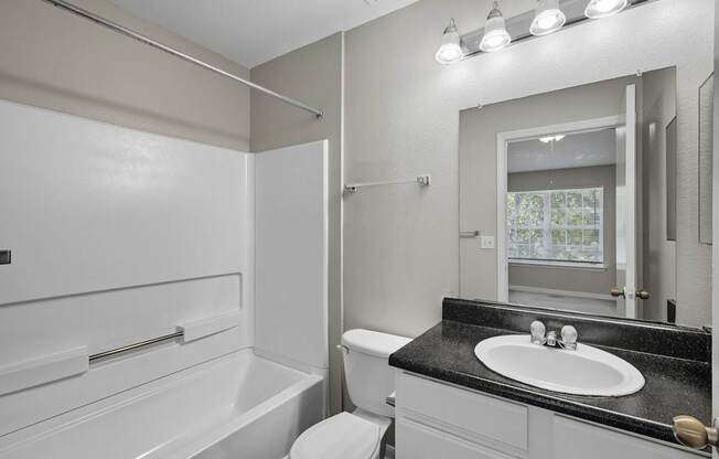 A white bathroom with a black countertop and a large mirror.