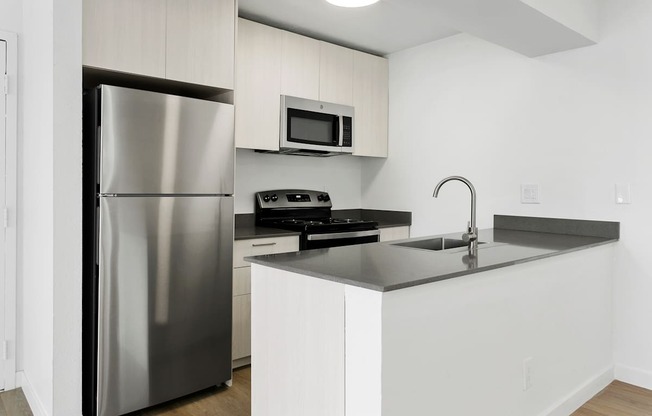 A modern kitchen with a stainless steel refrigerator and black countertops.