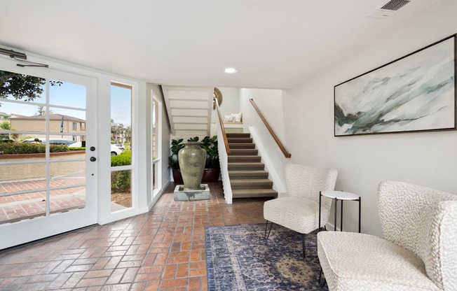 a living room with white chairs and a staircase and a glass door