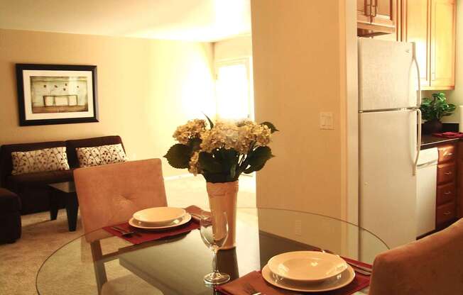 a kitchen and dining room with a glass table and a vase of flowers