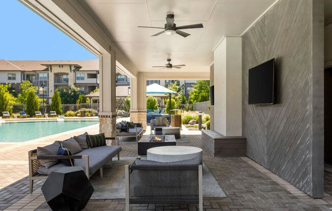 A modern outdoor patio area with a pool, seating, and a ceiling fan.