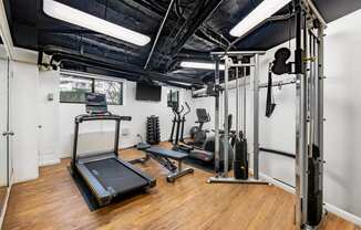 a gym with exercise equipment and weights in a room with white walls and wood floors