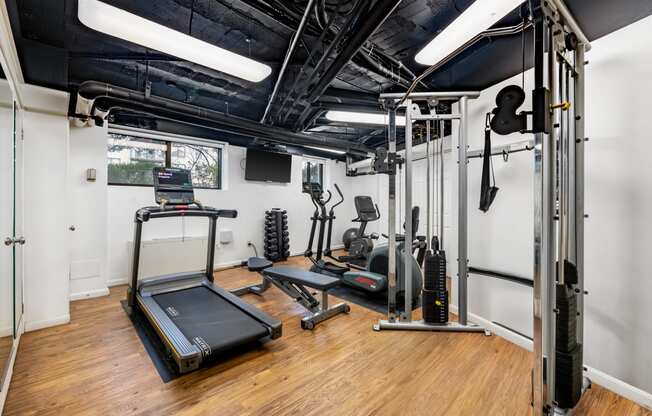 a gym with exercise equipment and weights in a room with white walls and wood floors