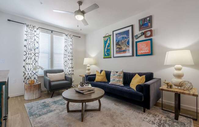 A living room with a blue couch, a grey armchair, a coffee table, and pictures on the wall.