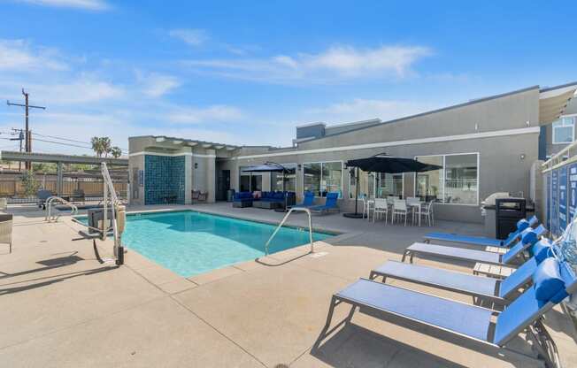 a swimming pool with lounge chairs and umbrellas in front of a building at Loma Villas Apartments, San Bernardino, CA