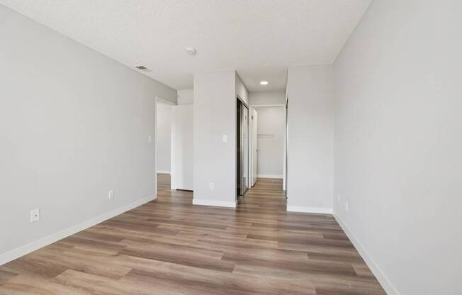 A long, empty hallway with wood flooring and white walls.
