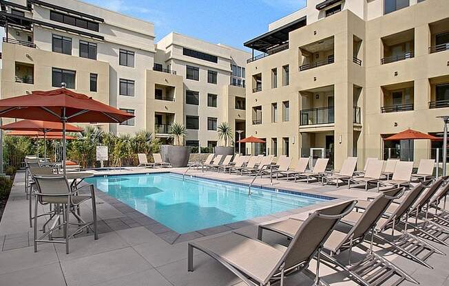 a swimming pool with chaise lounge chairs and umbrellas in front of an apartment building