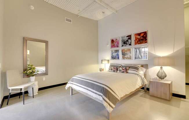A bedroom with a large bed, a chair, a mirror, and a wall-mounted lamp.