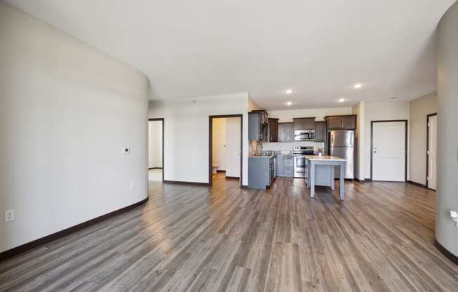 an empty living room and kitchen with wood floors and white walls