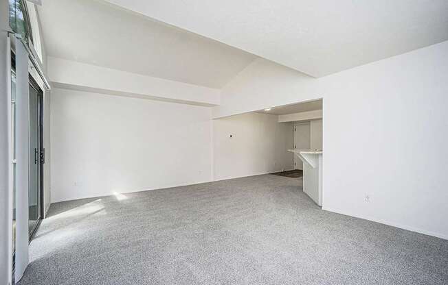 A large, empty living room with white walls and a grey carpet at Foxwood and The Hermitage in Portage, MI