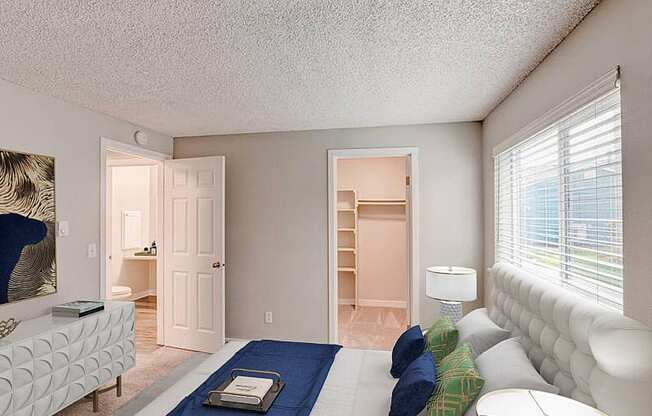 A bedroom with a spacious closet on the back wall and an oversized window above the queen-size bed.