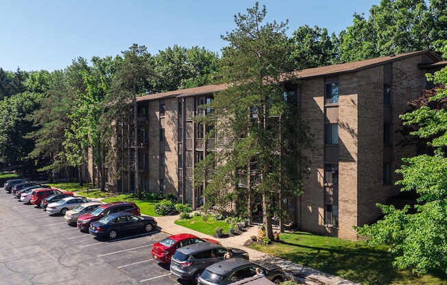 A parking lot with cars parked in front of a building with trees in the background.