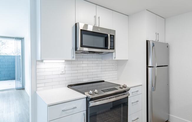 a kitchen with white cabinets and stainless steel appliances and a refrigerator at Avenue Two Apartments, California, 94063