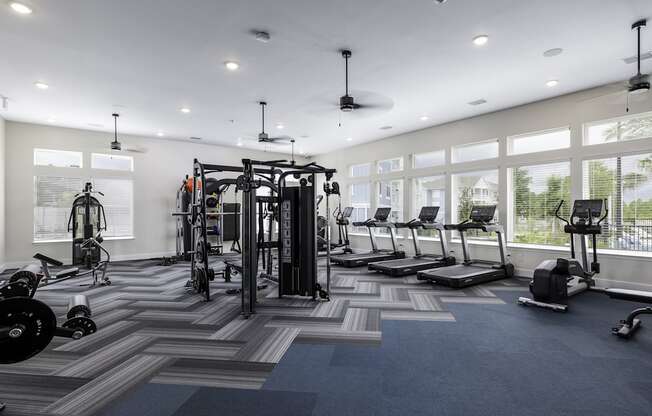 a gym with weights and cardio equipment in a building with large windows