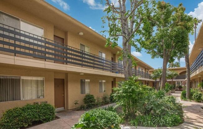 an apartment building with a courtyard and trees at Villa La Paz Apartments, Bellflower, California