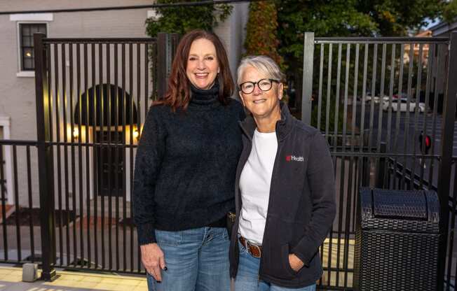 two women standing next to each other in front of a fence