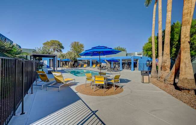 A pool area with a blue umbrella and yellow chairs.