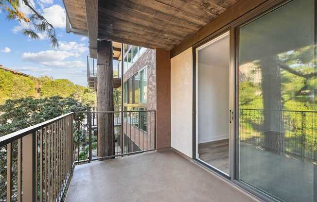 A balcony with a glass door and a view of trees.