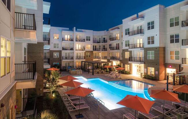 A swimming pool surrounded by orange umbrellas and chairs in a courtyard at night.