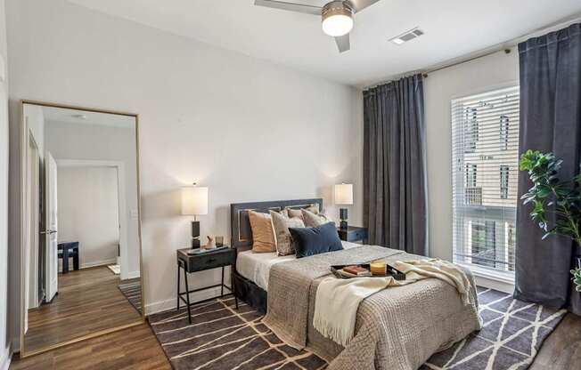 A bedroom with a large bed, a ceiling fan, and a view of a building outside the window.