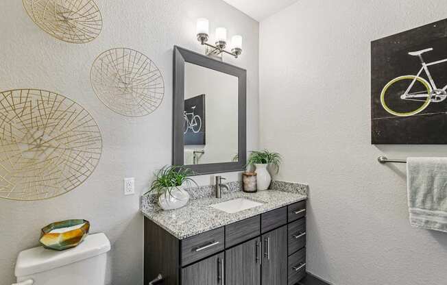 A bathroom with a white toilet, a sink with a mirror above it, and a bicycle drawing on the wall.