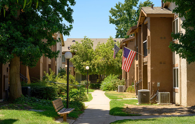 a pathway with a bench and trash cans in front of an apartment building at Oak Terrace Senior Apts, California, 92543