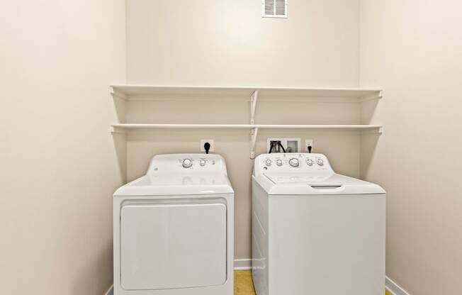 In-unit white washer and dryer set with shelving above and white walls at Sylvan Uptown,Colorado, Denver