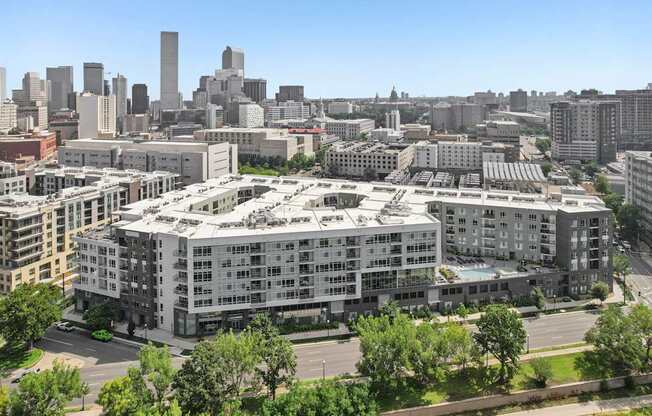 A large white building with a green roof is in the foreground of a cityscape.