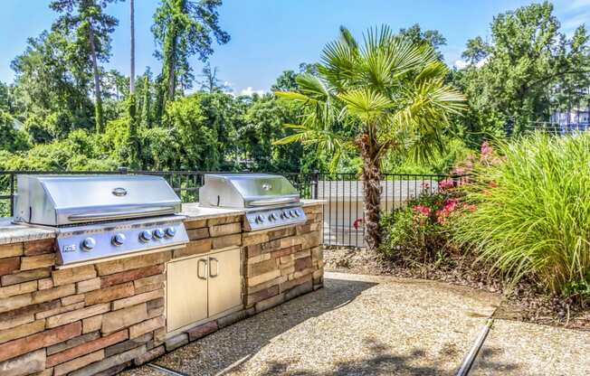 two gas grills on a brick wall in a backyard with trees