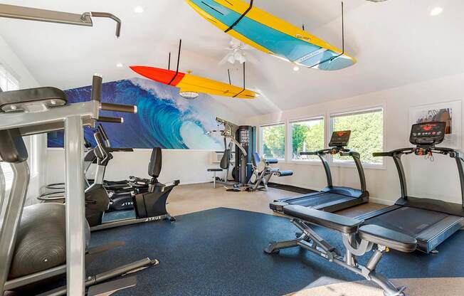 a gym with cardio equipment and a surfboard on the ceiling