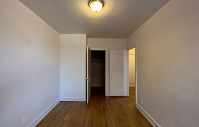 a bedroom with white walls and wood floors and a closet