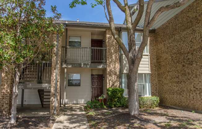 Front view of apartment building with trees and a pathway at Chisholm Place Apartments in Plano, TX